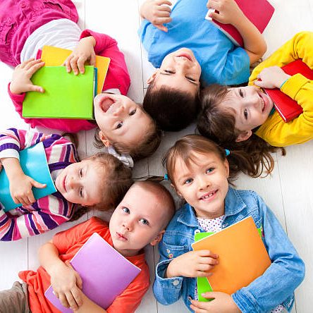 Six  kids with books lying  on the floor together. Top view