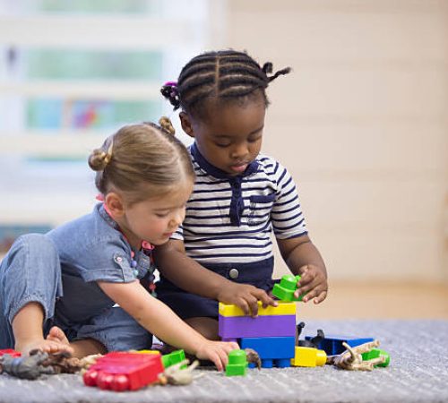 A multi-ethnic group of preschoolers are playing with plastic blocks together in class.